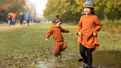 Two children wearing orange clothes jumping in puddles, having fun on a wet day.